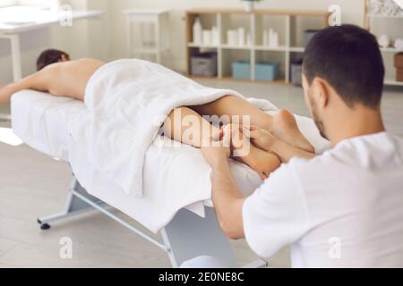 Uomo Masseur chiropractor in bianco uniforme massaggiando mentendo rilassanti donne tacchi Foto Stock