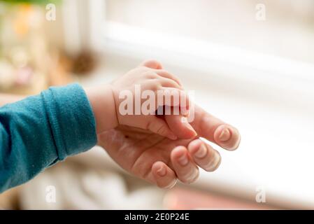 La madre usa la sua mano per tenere la mano minuscola del suo bambino per fargli sentire il suo amore, caldo e sicuro.amore di famiglia Foto Stock