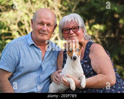 Uomo anziano e donna seduti insieme al piccolo cane Jack Russell terrier sulle mani, sorridendo Foto Stock