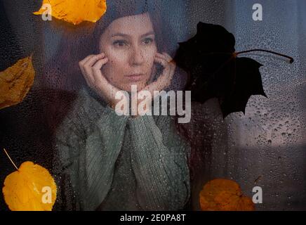 la donna è triste e guarda attraverso il vetro bagnato Foto Stock