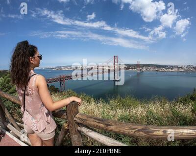 Il ponte sospeso rosso di Lisbona in una giornata di sole con la città sullo sfondo ponte portoghese simile al ponte di San Francisco, con una donna a t Foto Stock