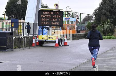 Southend-on-Sea, Regno Unito. 02 gennaio 2021. Un Jogger passa accanto a un cartello che dice 'Covid-19 Tariffe High SOS-Tier 4 Stay Safe' sul fronte del mare di Southend vicino al parco giochi 'Adventure Island'. Credit: Sport in Pictures/Alamy Live News Foto Stock