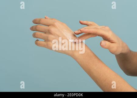 Donna che applica crema protettiva sulla pelle secca delle mani in stagione fredda, isolato su studio blu Foto Stock