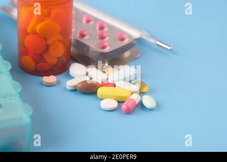 molte pillole colorate, termometro e blister su sfondo blu Foto Stock