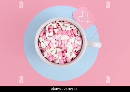 Tazza da tè riempita con cuori di zucchero rosa e bianco e. etichetta con il cuore su sfondo rosa Foto Stock