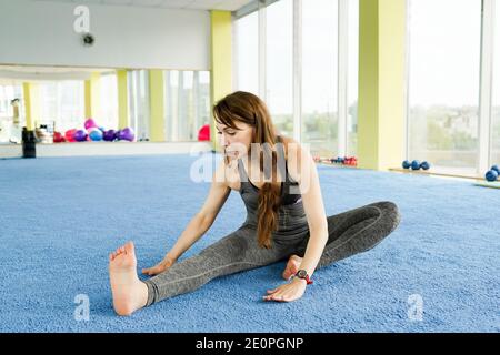 Tempo per lo yoga. Attraente giovane donna che si esercita e si siede sul pavimento in palestra. Concetto di stile di vita sano . Foto Stock