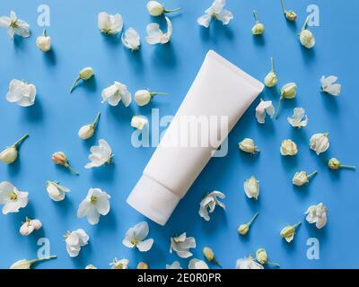 Tubo di plastica bianco per marcare a caldo e fiori bianchi piccoli su uno sfondo blu saturo. PRODOTTI cosmetici SPA. Fiore piatto posare e mock up. Vista dall'alto Foto Stock