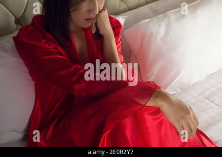 La triste donna penosa nella notte rossa da notte. Disordine di salute mentale guardando fuori la finestra da sola. Autoisolamento Foto Stock