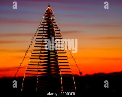 Tramonto con albero di Natale creato con bastoni di legno e decorato con lampadine colorate Foto Stock