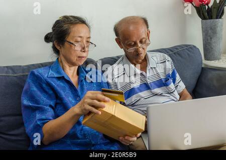 Due persone asiatiche anziane che acquistano online. Senior che tiene la carta di credito seduto su un divano con il computer portatile a casa. Foto Stock