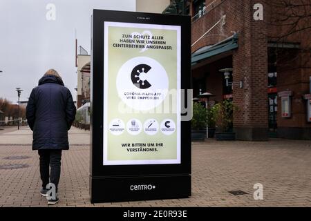 Centro, Oberhausen, NRW, Germania. 02 gennaio 2021. Una donna oltrepassa un banner che consiglia l'uso dell'applicazione di avvertimento Corona e delle regole di allontanamento sociale. Il più grande centro commerciale della Germania e i ristoranti, i caffè e i divertimenti circostanti appaiono sgarbati e desertati, le entrate sono chiuse e chiuse. Il popolare centro commerciale con 125.000 m² di spazio commerciale e l'intera area all'aperto sarebbe normalmente un grande paradiso per gli acquirenti alla ricerca di occasioni nelle vendite di gennaio. Credit: Imageplotter/Alamy Live News Foto Stock