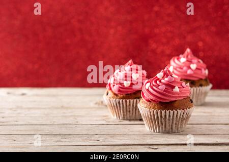 Cupcake decorati con cuori di zucchero per San Valentino in legno tabella e sfondo rosso Foto Stock