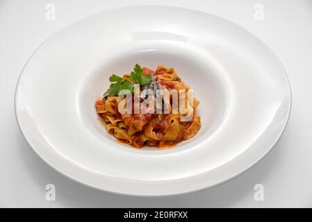 Tagliatelle con salsa di pomodoro rosso, acciughe e foglie di prezzemolo, tipica pasta italiana all'uovo in piatto bianco su fondo bianco Foto Stock