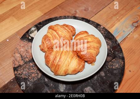 Un piatto di tre croissant appena fatti su un piatto in una cucina su un piano di lavoro in legno Foto Stock