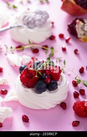 Torta di meringa Pavlova con frutti di bosco su fondo rosa zucchero polverato Foto Stock