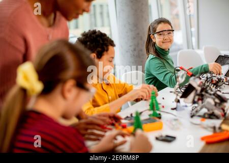 Smily African American insegnante di scienza femminile con gruppo di bambini programmazione di giocattoli e robot elettrici in classe robotica Foto Stock