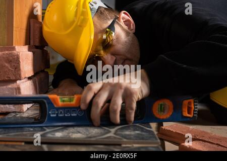 Molto vicino. Durante la posa della terracotta, l'operaio generale controlla la correttezza dell'esecuzione con una livella a spirito. Un dipendente che indossa dispositivi di protezione individuale. Foto Stock