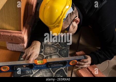 Durante la posa della terracotta, l'operaio generale controlla la correttezza dell'esecuzione con una livella a spirito. Un dipendente che indossa dispositivi di protezione individuale. Foto Stock