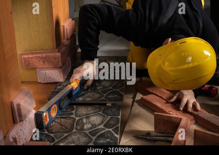 Durante la posa della terracotta, l'operaio generale controlla la correttezza dell'esecuzione con una livella a spirito. Un dipendente che indossa dispositivi di protezione individuale. Foto Stock