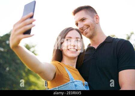 Giovane felice millennial coppia sorridente e prendendo selfie - Z Generazione di turisti che si divertono insieme - concetto di tecnologia con un smartphone e amici Foto Stock