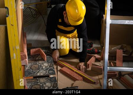 Un esperto addetto alla costruzione, che indossa indumenti protettivi e un casco, misura le piastrelle decorative prima di attaccarle. Foto Stock