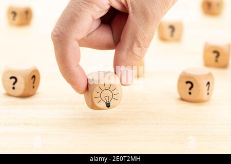 Idea creativa o concetto di innovazione. Blocco cubo di legno selezionato a mano con il simbolo del punto interrogativo e l'icona della lampadina sul tavolo di legno Foto Stock