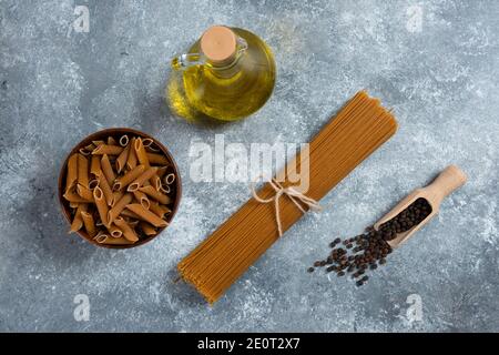 Due tipi di pasta cruda e una bottiglia di vetro di olio Foto Stock