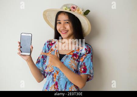 Felice viaggiatore asiatico donna dimostrare cellulare. Ritratto di ragazza sorridente, che posa su sfondo bianco Foto Stock