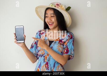 Felice viaggiatore asiatico donna dimostrare cellulare. Ritratto di ragazza sorridente, che posa su sfondo bianco Foto Stock