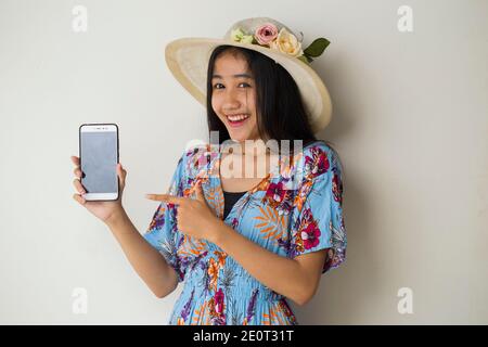 Felice viaggiatore asiatico donna dimostrare cellulare. Ritratto di ragazza sorridente, che posa su sfondo bianco Foto Stock