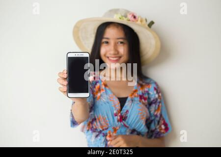 Felice viaggiatore asiatico donna dimostrare cellulare. Ritratto di ragazza sorridente, che posa su sfondo bianco Foto Stock