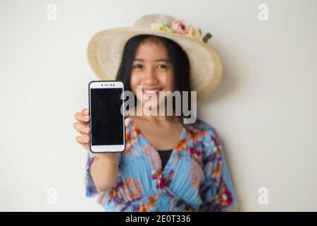 Felice viaggiatore asiatico donna dimostrare cellulare. Ritratto di ragazza sorridente, che posa su sfondo bianco Foto Stock