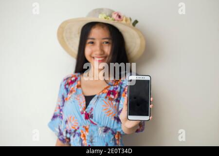 Felice viaggiatore asiatico donna dimostrare cellulare. Ritratto di ragazza sorridente, che posa su sfondo bianco Foto Stock