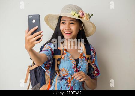 Felice viaggiatore asiatico donna dimostrare cellulare. Ritratto di ragazza sorridente, che posa su sfondo bianco Foto Stock