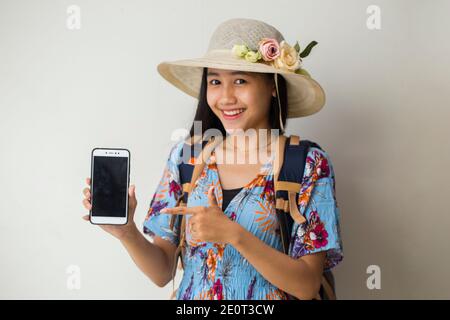 Felice viaggiatore asiatico donna dimostrare cellulare. Ritratto di ragazza sorridente, che posa su sfondo bianco Foto Stock