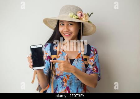 Felice viaggiatore asiatico donna dimostrare cellulare. Ritratto di ragazza sorridente, che posa su sfondo bianco Foto Stock