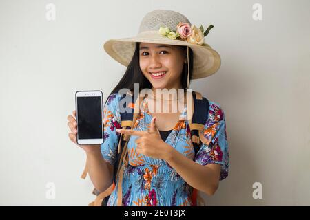 Felice viaggiatore asiatico donna dimostrare cellulare. Ritratto di ragazza sorridente, che posa su sfondo bianco Foto Stock