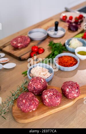 Chef che prepara polpette e le mette su una tavola di legno. Ci sono varie spezie, verdure, così come piccole bocce da cucina intorno al lavoro surf Foto Stock