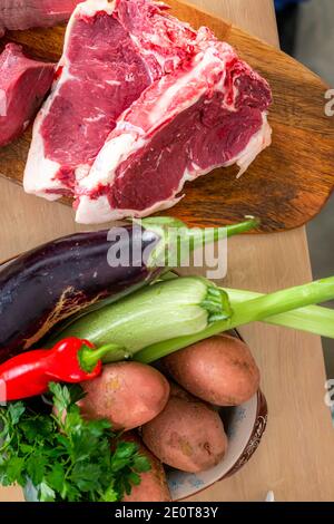 Pezzi di carne e di accompagnamento spezie e verdure fotografate su una tavola di legno sulla superficie di lavoro della cucina. Foto Stock