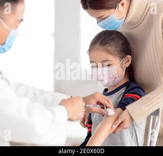 medico che esamina il bambino e dà l'iniezione. Vaccinazione con coronavirus e concetto di vaccino Covid-19 Foto Stock