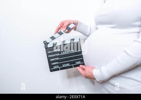 Donna incinta mani tenendo clapper bordo sul suo ventre. Con cartello di caricamento Foto Stock