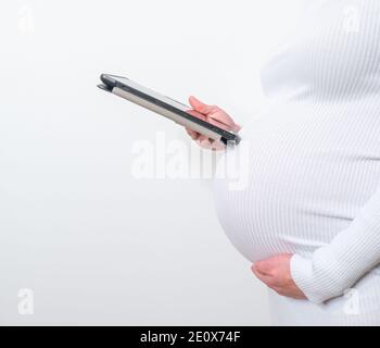 Contenuto donna incinta che tiene la sua tavoletta stanting in vita camera a casa Foto Stock