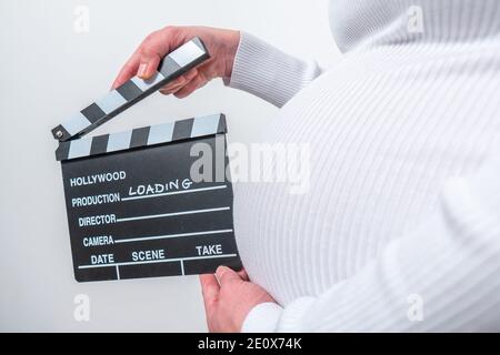 Donna incinta mani tenendo clapper bordo sul suo ventre. Con cartello di caricamento Foto Stock