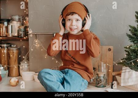 Ragazzo in cucina che ascolta la musica con le cuffie wireless. L'adolescente si divertirà a casa, in cucina. Vacanza a casa. Foto Stock