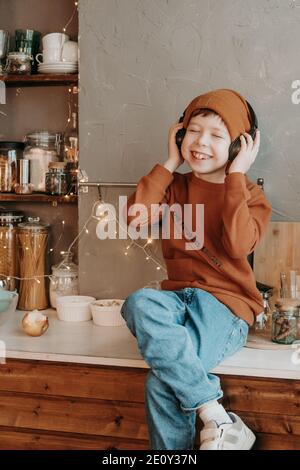 Ragazzo in cucina che ascolta la musica con le cuffie wireless. L'adolescente si divertirà a casa, in cucina. Vacanza a casa. Foto Stock