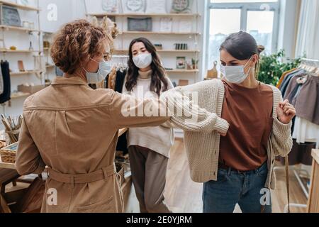 Due giovani donne in un negozio ecologico si salutano a vicenda, toccando i gomiti Foto Stock