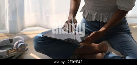 Primo piano dell'illustratrice di un artista donna che si sta disegnando su un tablet digitale con penna stilo mentre si è seduti a terra. Foto Stock