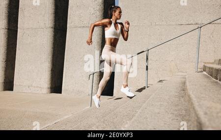 donna fitness che corre sui gradini. Immagine laterale di una atleta runner che sale le scale. Foto Stock