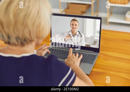 Donna anziana seduto al computer portatile e che parla con un medico virtuale del servizio e-health Foto Stock