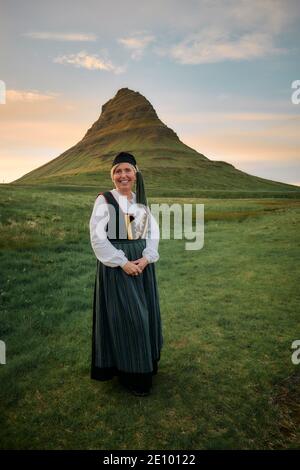 Donna islandese locale che indossa Upphlutur tradizionale abito nazionale con cappuccio di coda, Kirkjufell Kirkjufellsfoss a Grundarfjörður, Snæfellsnes, Islanda Foto Stock